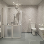 A modern wet room with a showerhead, toilet, and sink. The shower floor slopes gently towards a drain.