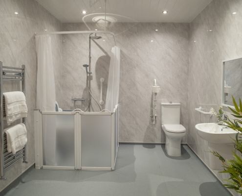A modern wet room with a showerhead, toilet, and sink. The shower floor slopes gently towards a drain.